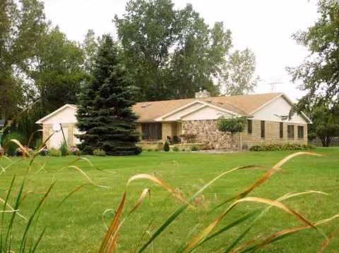 Single-story brick-and-stone residence with a green lawn and surrounding trees.