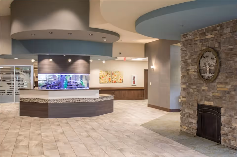 Modern reception lobby with a central desk featuring an aquarium, a stone fireplace on the right, and decorative ceiling elements.