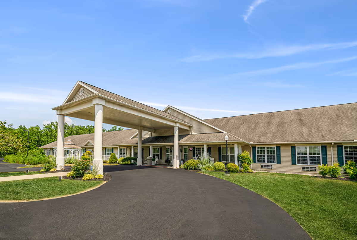 Single-story senior living facility exterior with a covered porte-cochère entrance, landscaped grounds, and a blue sky.