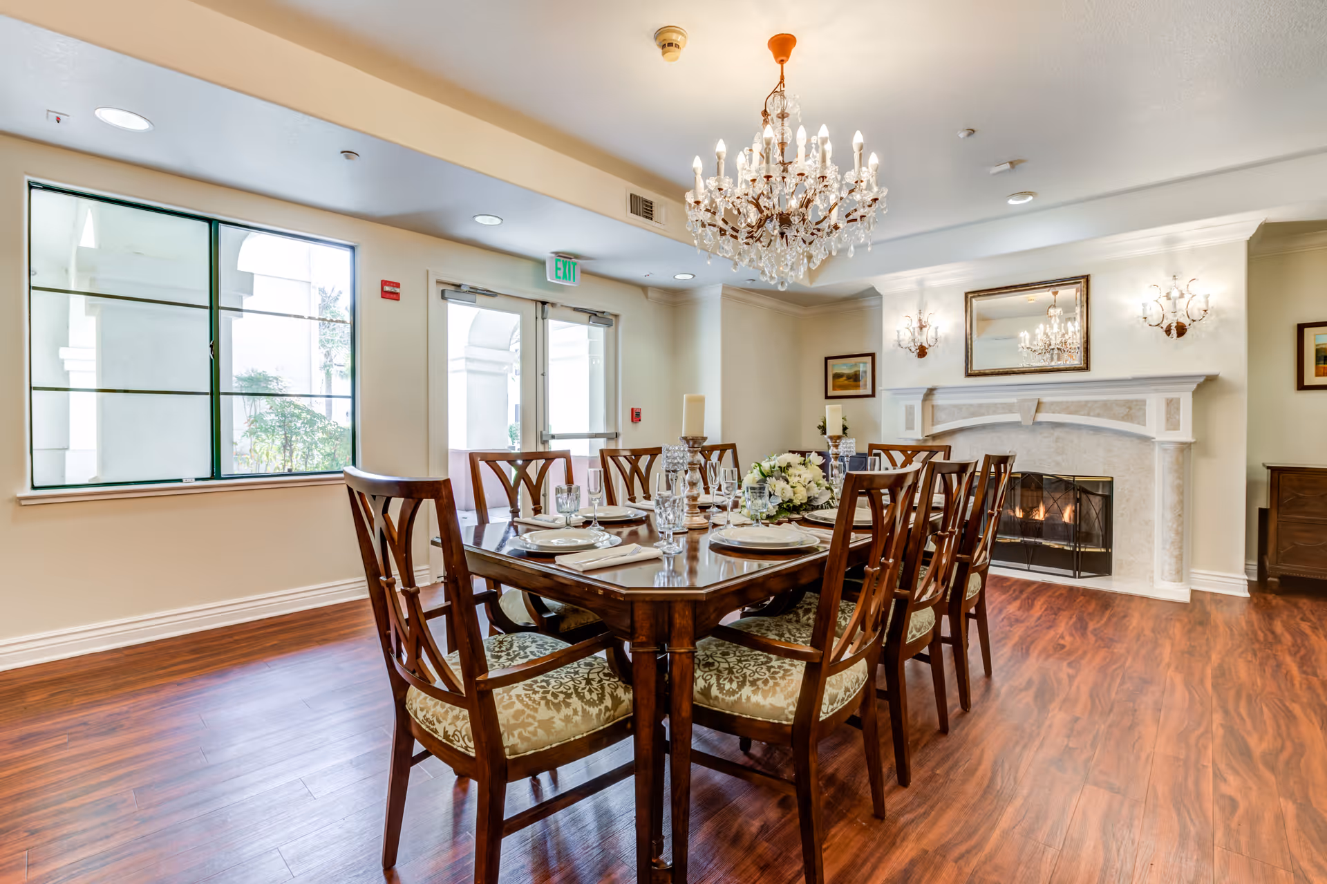 Elegant dining room with a wooden table set for dinner, crystal chandelier and a lit fireplace.