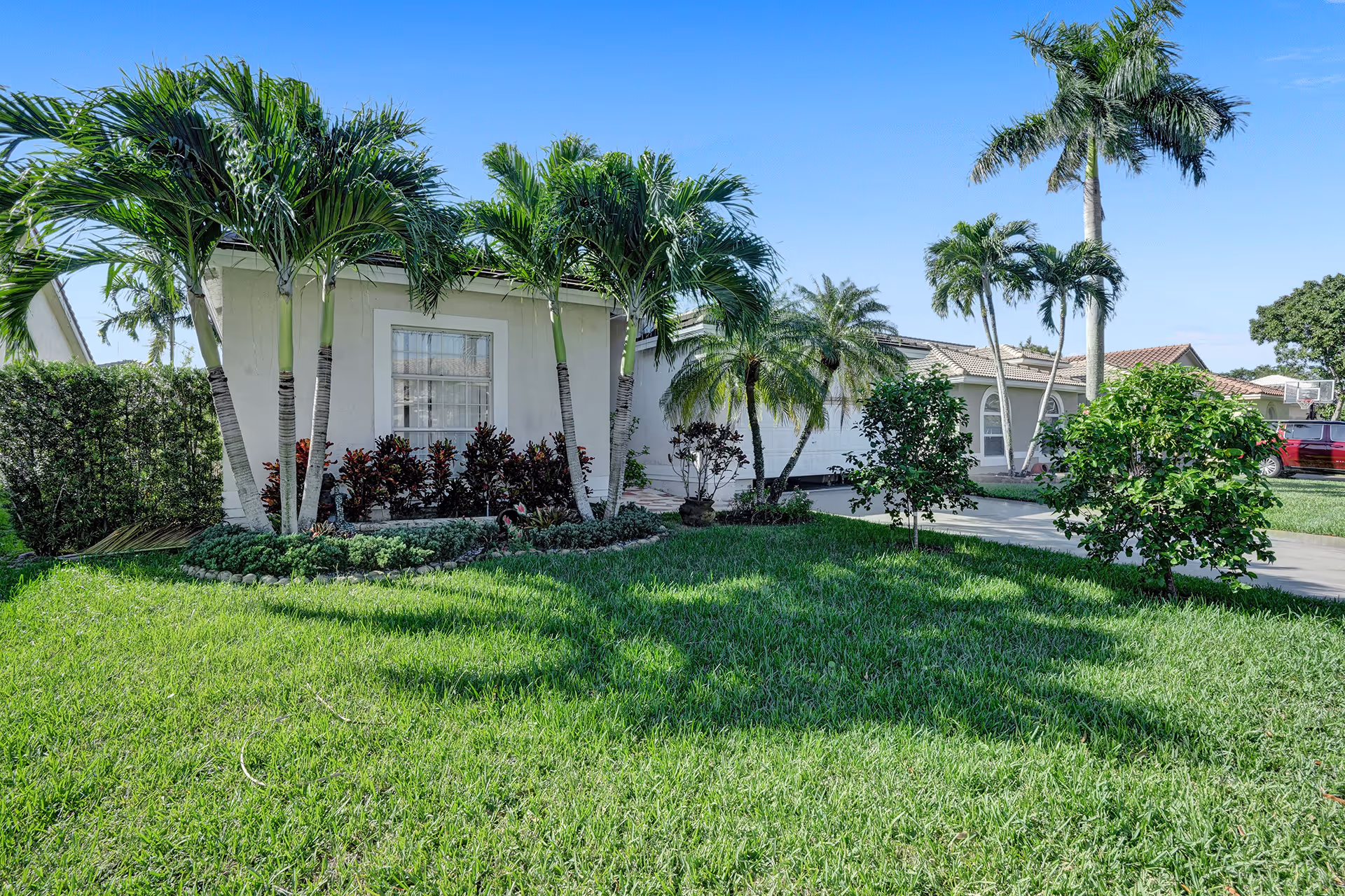 Exterior view of a single-story residential building with a well-maintained lawn and various palm trees and shrubs under a clear blue sky.