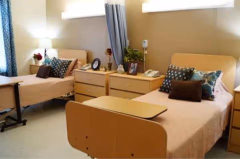 Two single beds with nightstands and a privacy curtain in a shared senior living bedroom.