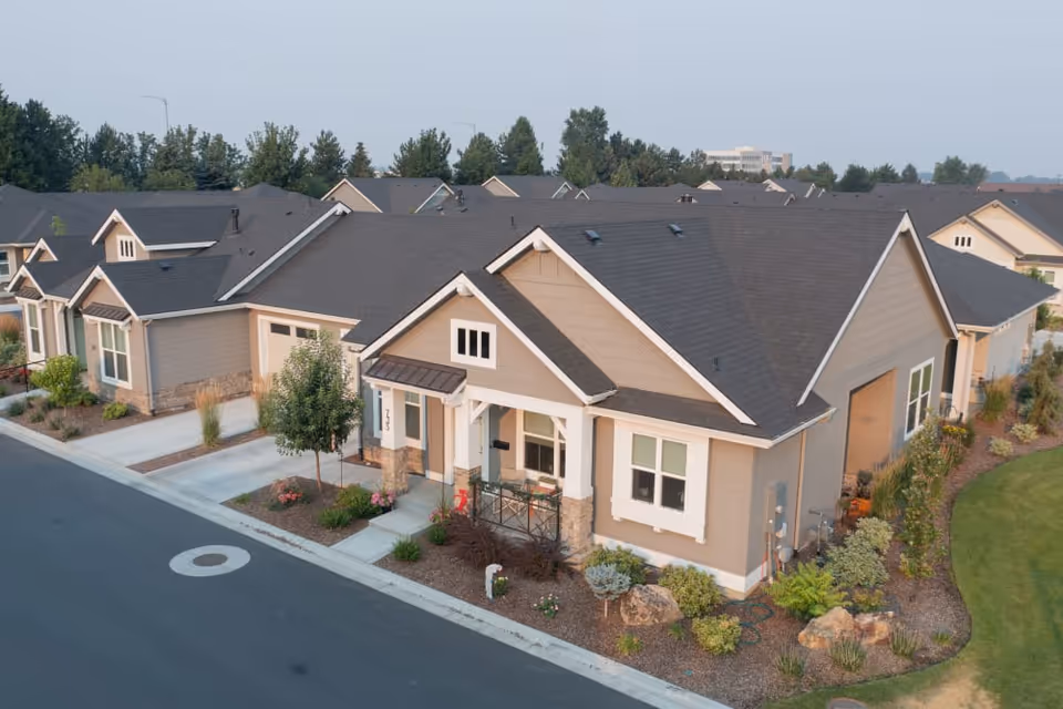 Aerial view of single-story beige ranch-style homes with landscaped front yards and driveways in a residential community.