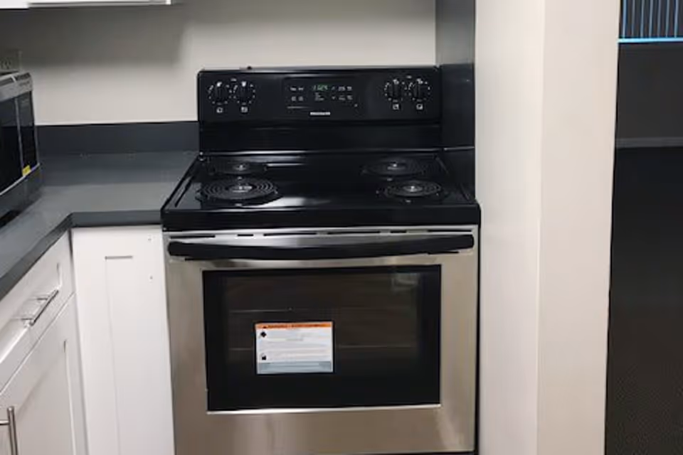 A modern kitchen corner featuring a stainless steel electric stove with four coil burners and an oven. The stove is set against a gray countertop with white cabinetry below and a microwave oven on the left side.