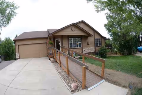 Front exterior of a single-story senior living home with a wooden ramp
