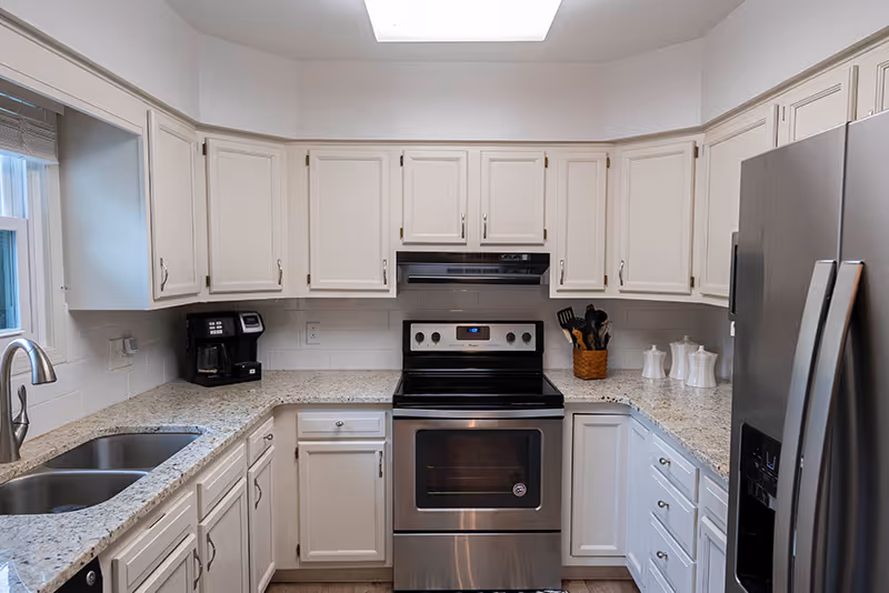 Bright U-shaped kitchen with white cabinets, granite countertops, a stainless steel stove and refrigerator, and a double sink.
