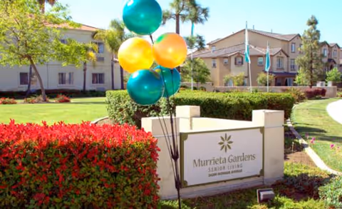 Outdoor view of Murrieta Gardens sign amid landscaping and buildings.