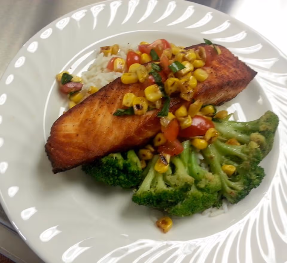 A plate with a seared salmon fillet served over rice with broccoli and a corn and tomato salsa.