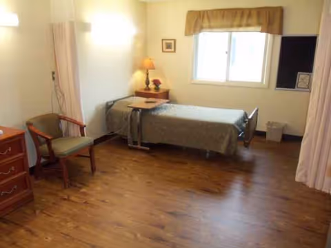 Senior living bedroom with bed, chair, dresser, lamp, and window.