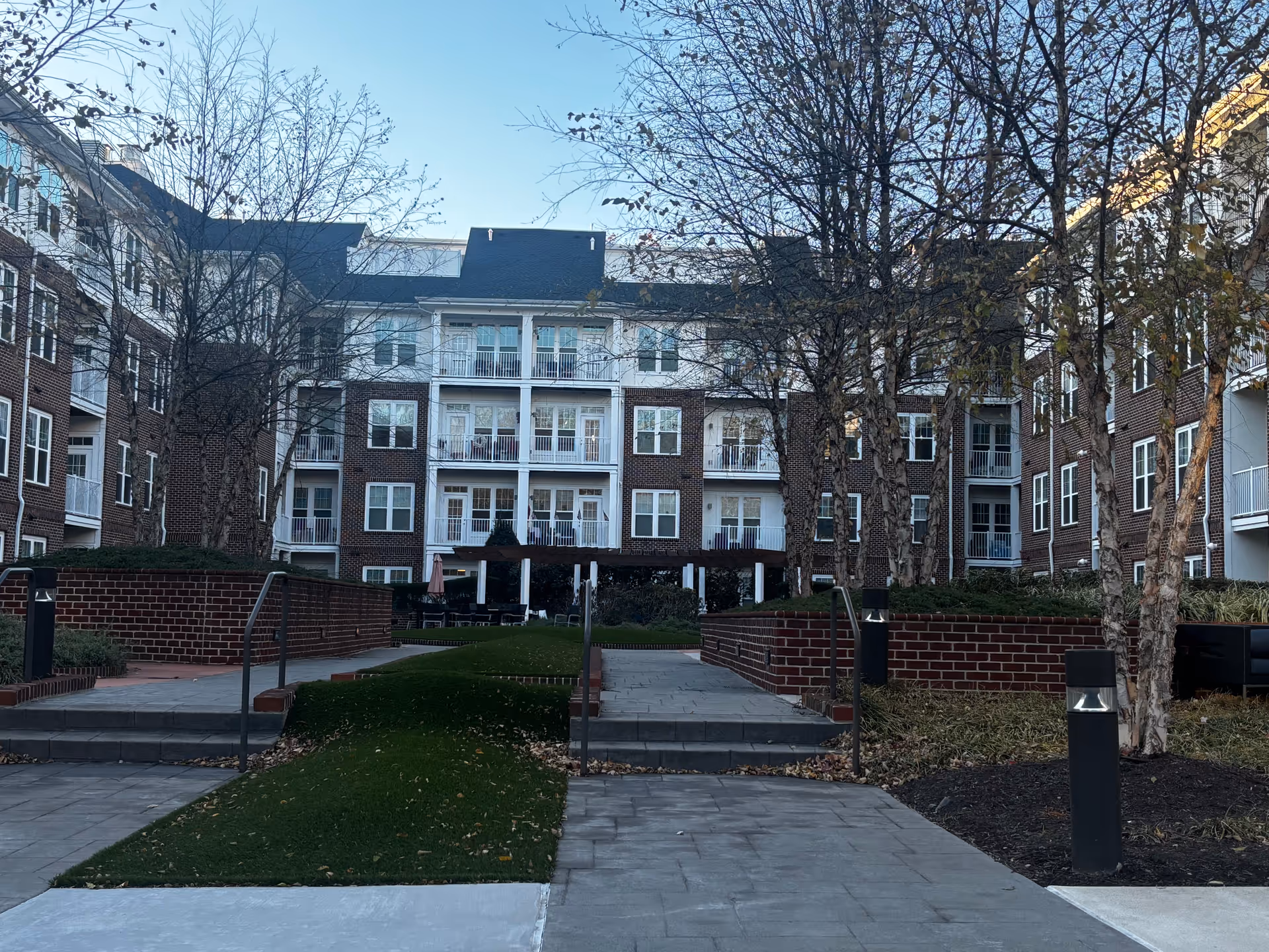 Courtyard view of a multi-story brick senior living building with balconies, walkways, trees, and raised brick planters.