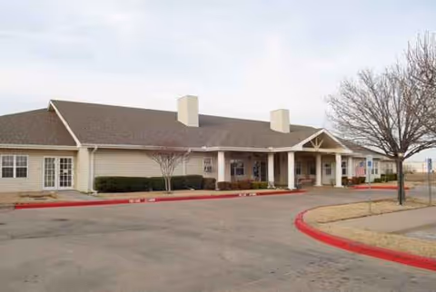 Single-story senior living facility with beige siding, entrance canopies, and a red-curbed driveway.