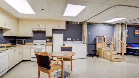 Interior of senior living facility showing a kitchenette with cabinets, appliances, and a small round table.