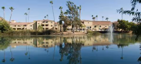 Savant of Jurupa Valley exterior with a lakeside fountain, palm trees, and a tan multi-building facility.