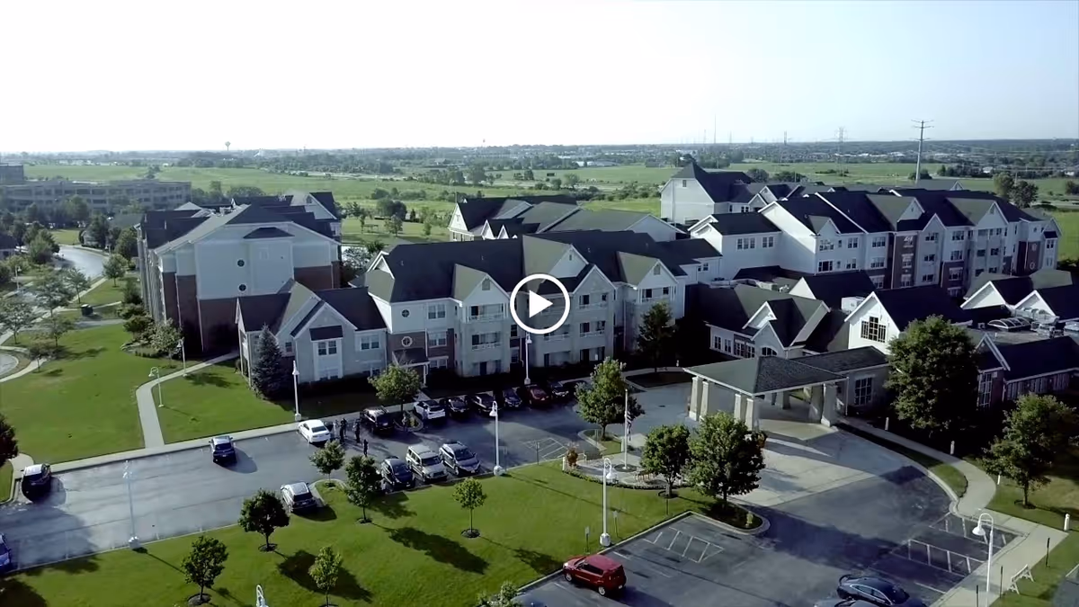 Aerial view of the Smith Crossing senior living complex showing multi-story residential buildings, an entrance canopy, parking lot, and surrounding green lawns.