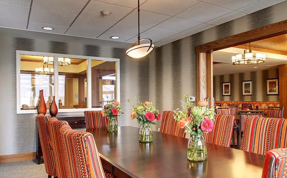 A dining room with a long wooden table, striped upholstered chairs and vases of fresh flowers.