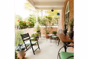 Covered front porch with potted plants, folding chairs and a small table along a brick exterior wall.