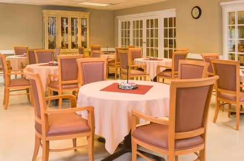 Round tables with pink tablecloths and wooden chairs arranged for dining in a quiet dining room.