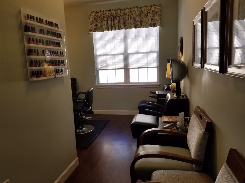 Small salon room with chairs, a hooded hair dryer, and a wall-mounted nail polish display near a window.