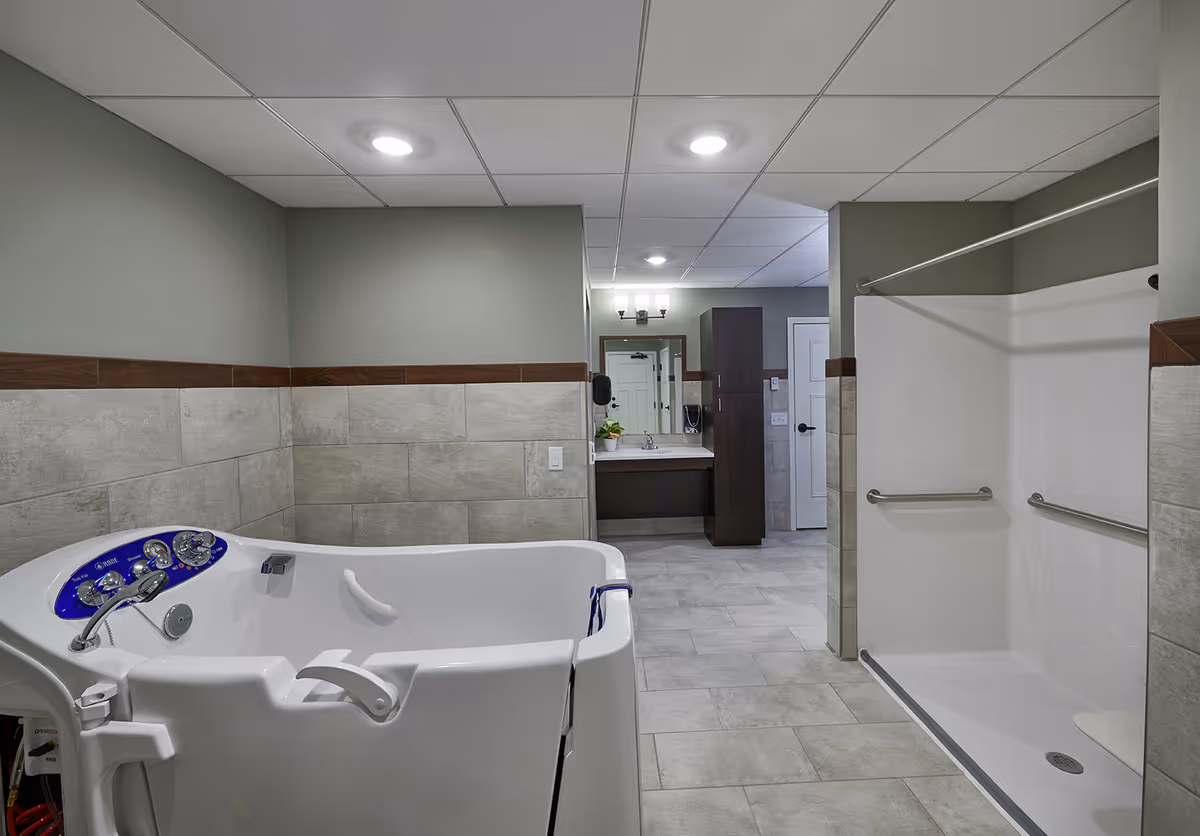 Accessible bathroom featuring a walk-in tub, an open roll-in shower with grab bars, and a vanity in the background.