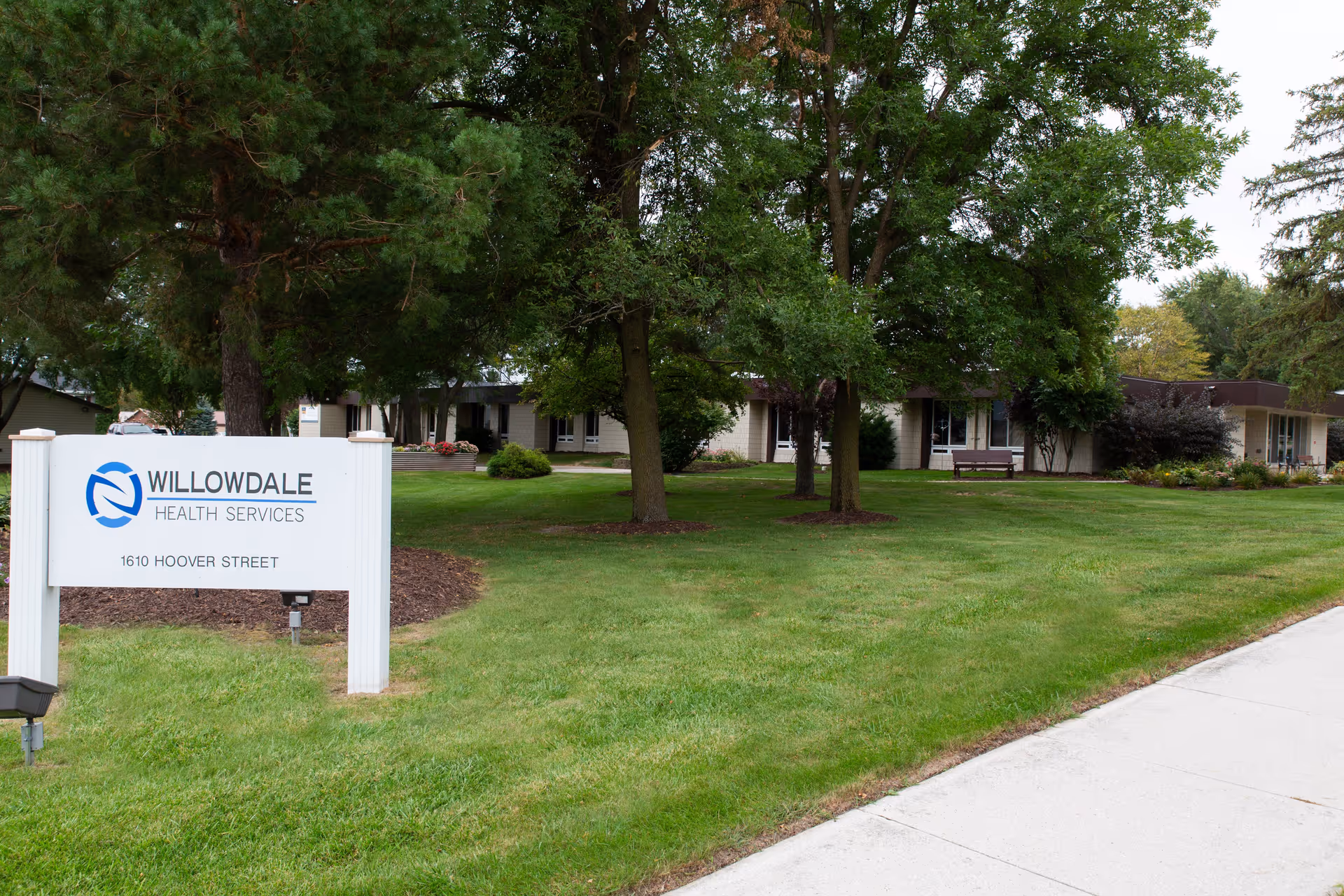 A Willowdale Health Services sign on a lawn in front of a one-story building surrounded by trees.