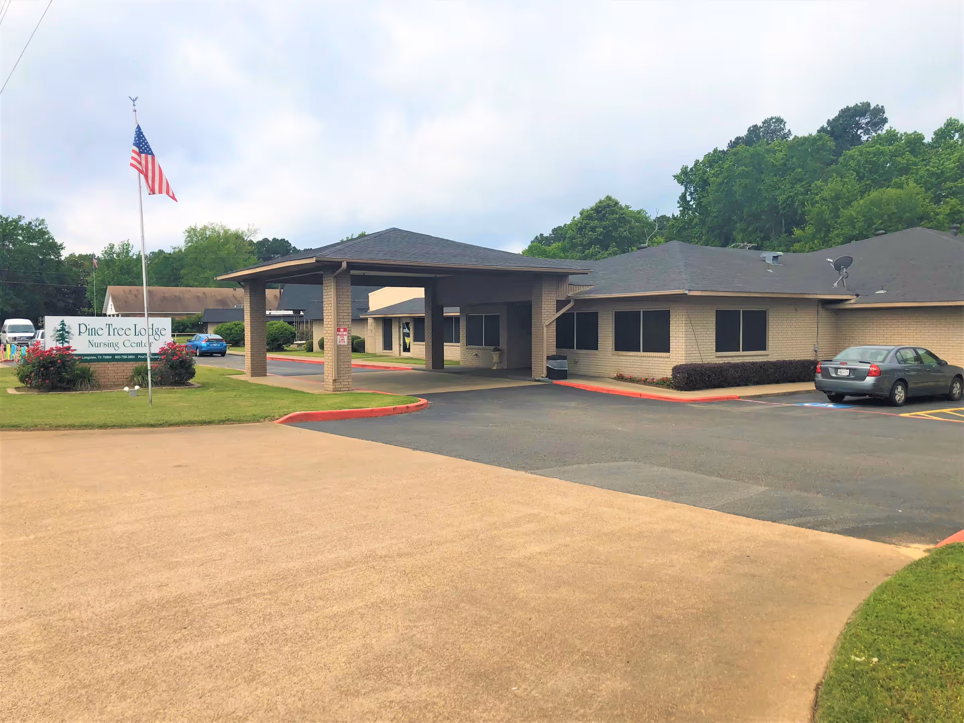 Exterior front entrance of Pine Tree Lodge Nursing Center showing a covered drop-off, sign, flagpole, and parking lot.