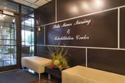Lobby entrance with cushioned benches, a planter, and a wall sign reading 'Stella Manor Nursing & Rehabilitation Center'.