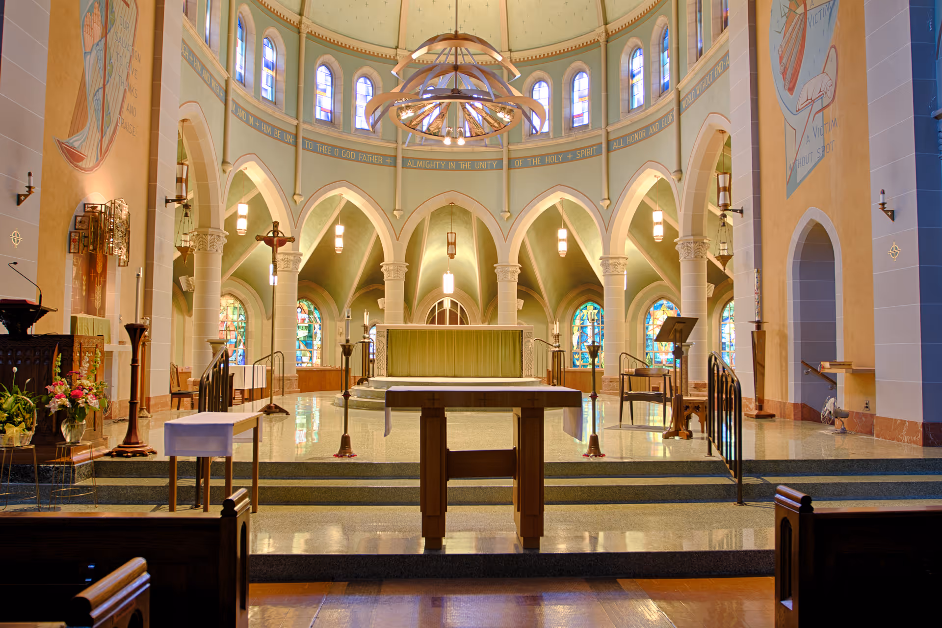 Interior view of a chapel with an altar, arched columns, stained-glass windows, and hanging chandeliers.