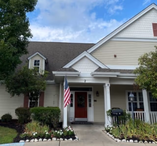 Front exterior of Tylers Mill Senior Living showing red door, porch, and American flag.