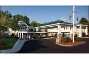 Front entrance of a two-story healthcare building with a porte-cochere, flagpoles, and landscaped driveway.