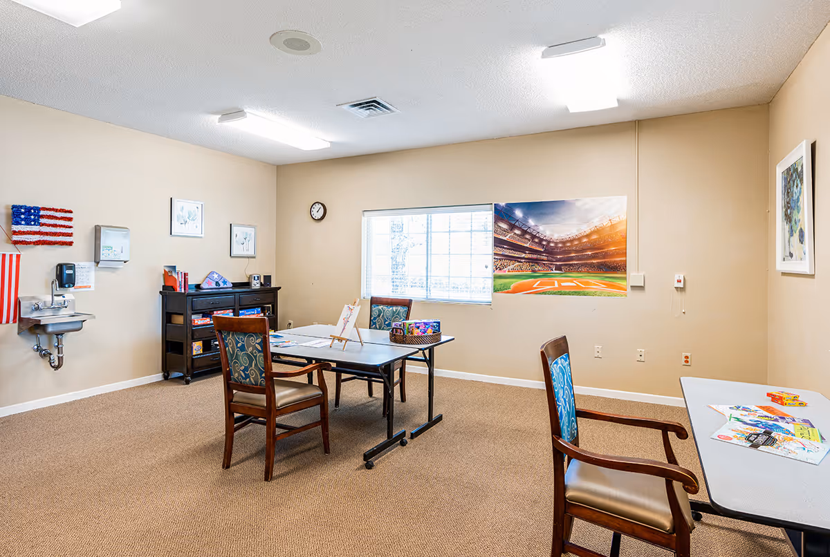Small activity room with tables and chairs, craft supplies, a sink, and a large baseball stadium poster on the wall.