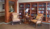 Cozy sitting area with two armchairs, a round side table, and built-in bookshelves filled with books.