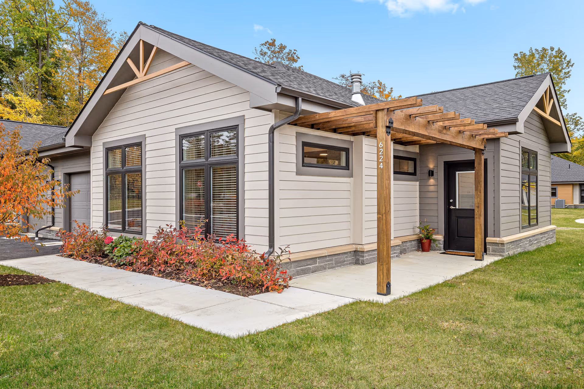 Exterior front entrance of a single-story modern cottage with a wooden pergola, large windows, and landscaped walkway.