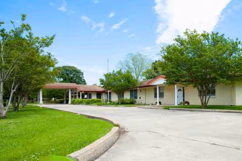 Exterior view of Colonial Nursing Home with a curved driveway and trees.