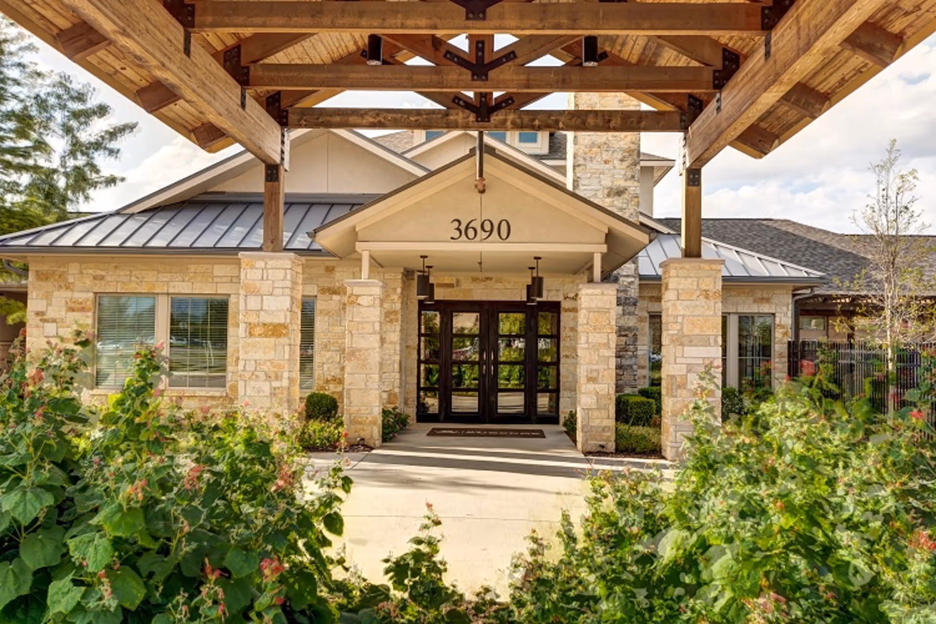 Stone-front entrance with a wooden porte-cochere, double glass doors and the address number 3690 above the doorway, framed by landscaping.