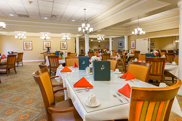Spacious dining room with tables set with white tablecloths, red napkins, green menus, and chandeliers.