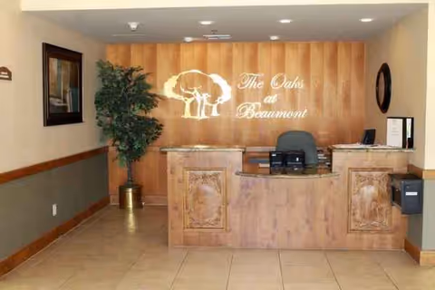 Reception desk with wooden panels, plants, and a wall sign reading The Oaks at Beaumont.
