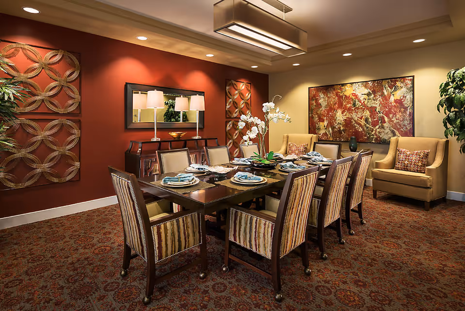 Dining room with a long set table for eight, striped upholstered chairs, decorative wall art, and warm ambient lighting.