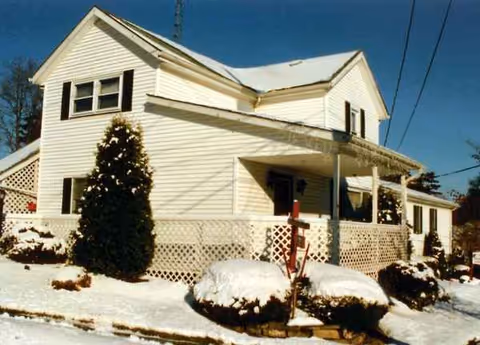 White two-story house with snow and a covered front porch.