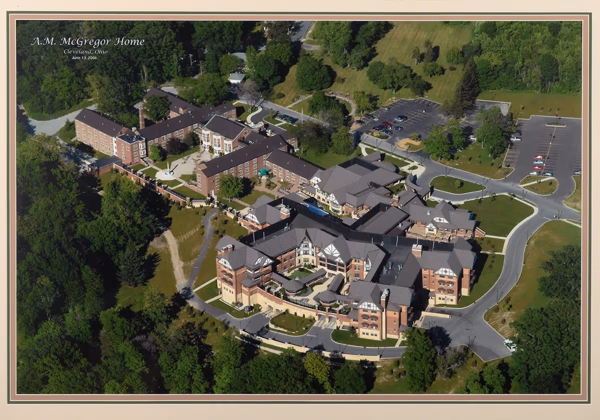 Aerial view of the A.M. McGregor Home, a large assisted living facility surrounded by trees and greenery. The complex consists of multiple connected buildings with parking lots and driveways, situated in a spacious, landscaped area.