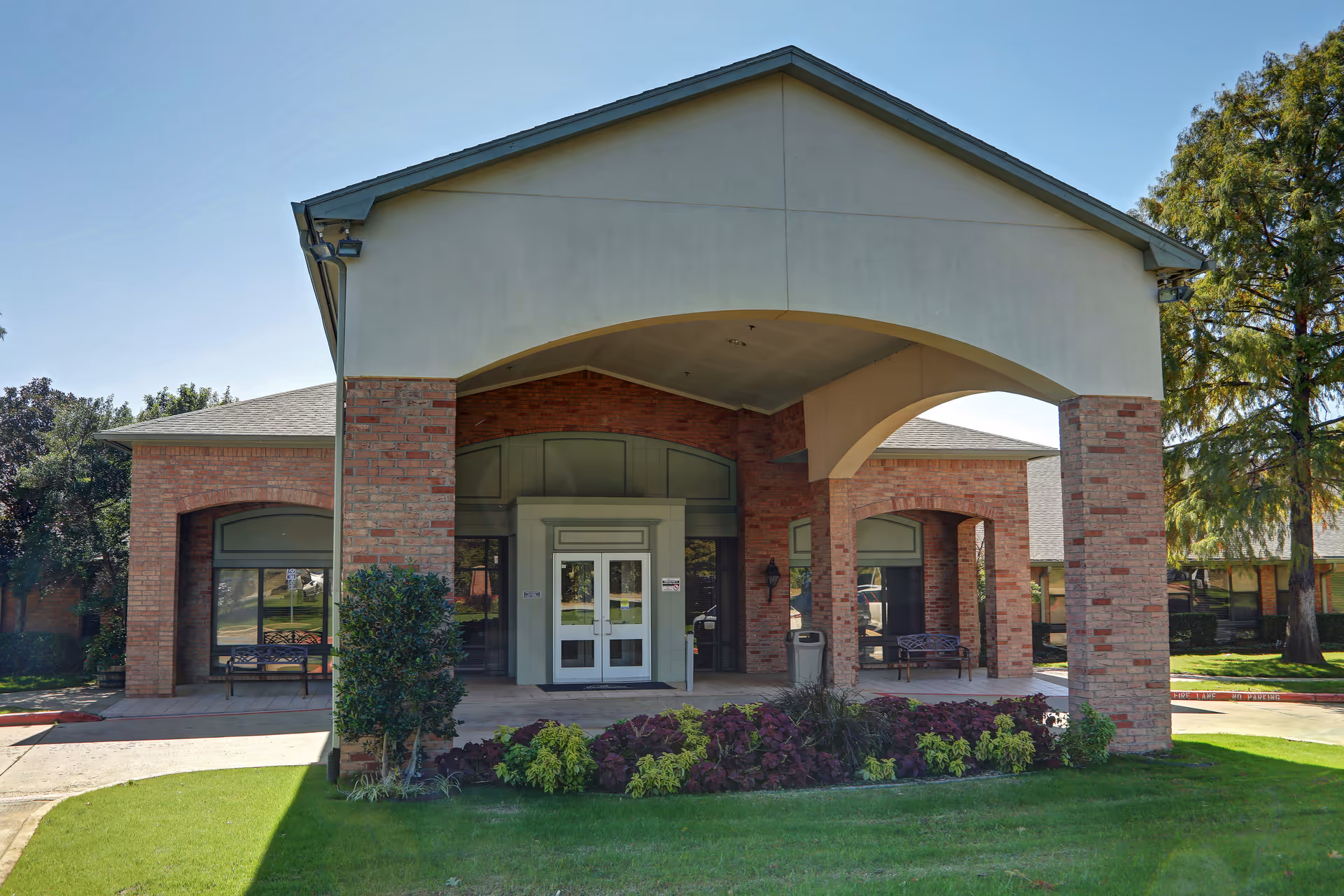 Front entrance of a brick senior living building with a covered portico, double glass doors and landscaped lawn.