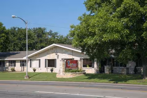 Single-story rehabilitation facility with stone facade, sign, and green lawn along a street.