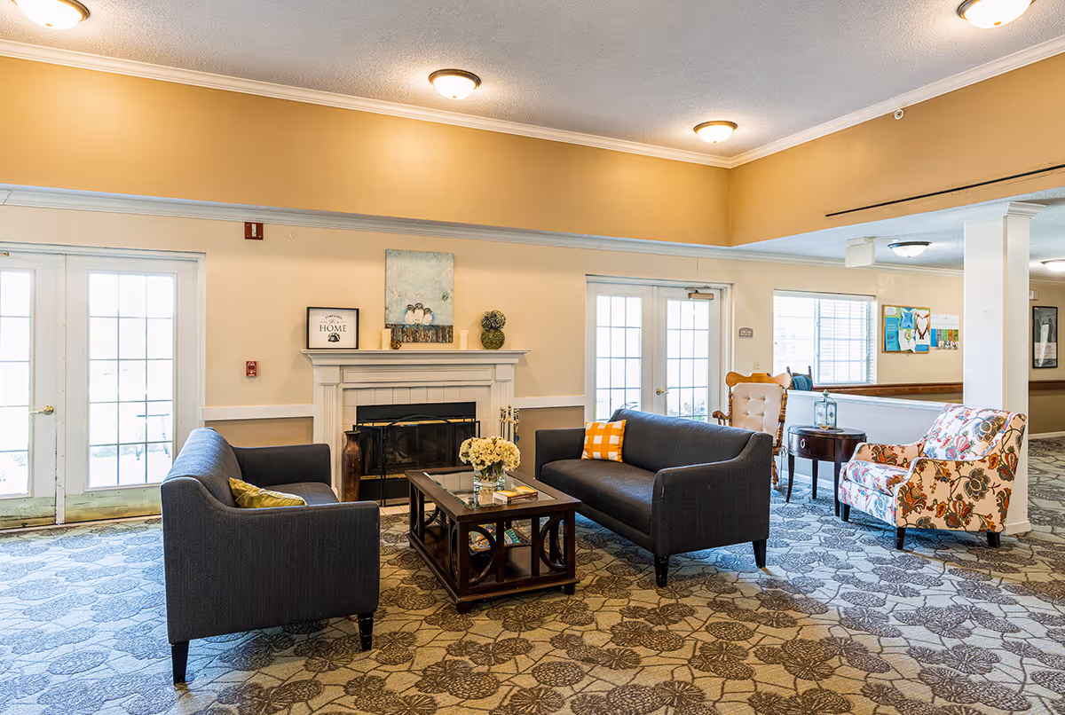 Bright, well-furnished living room/lounge with sofas, armchairs, a fireplace and a coffee table on patterned carpet.