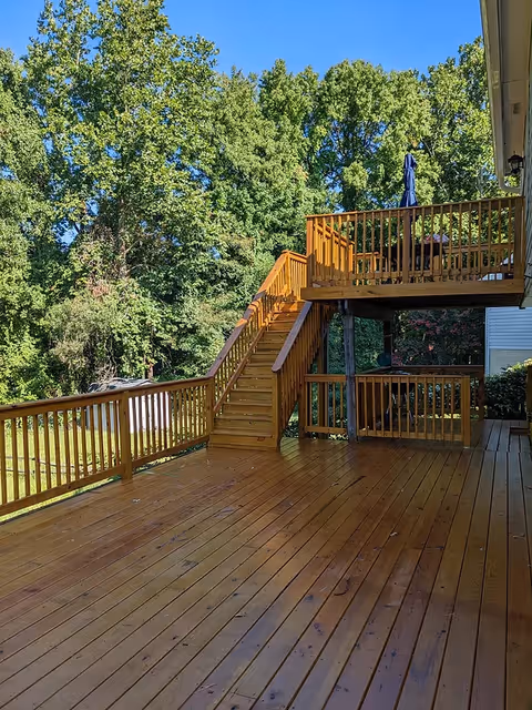 Wooden two-level outdoor deck with stairs and railings, an upper deck with a table umbrella, and trees in the background.