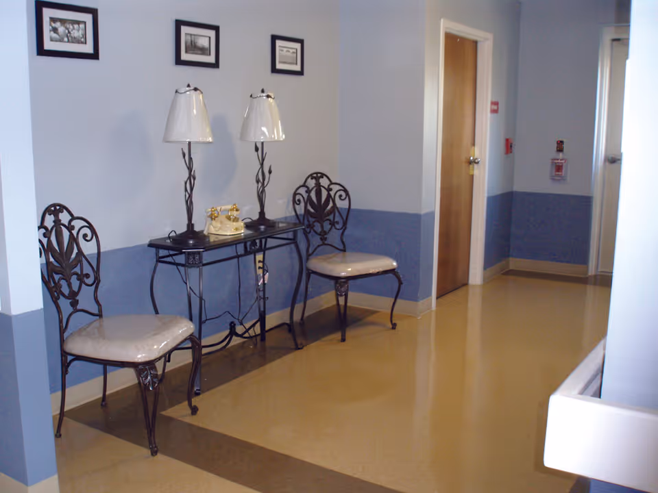 A small seating area in a hallway with two decorative chairs, a narrow console table holding two lamps and a vintage telephone against a pale blue wall.