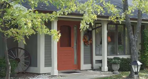 Front entrance of a senior living building with a red door, wreath, and porch.