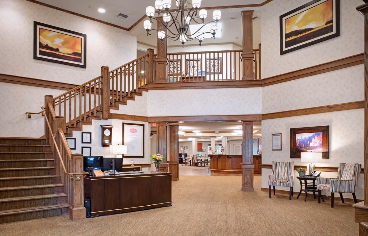 Spacious two-story reception lobby with a wooden staircase, front desk, seating area, and chandelier.
