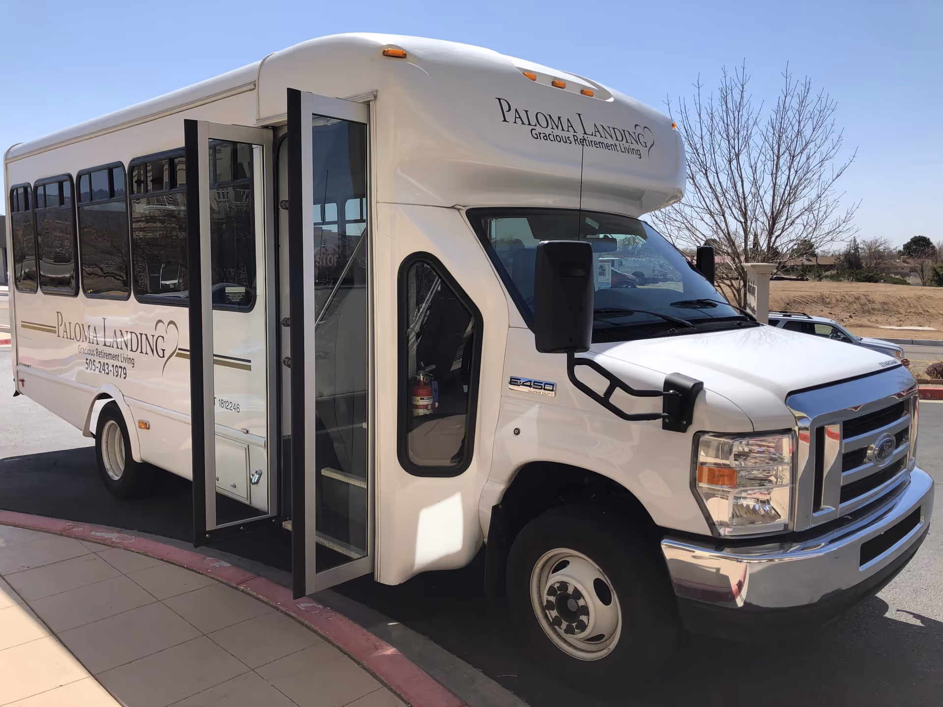 A white Paloma Landing retirement community shuttle bus parked outside with its passenger door open.