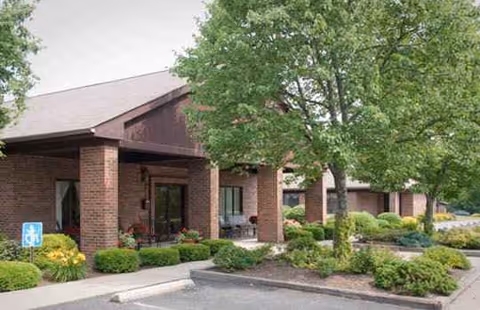Brick senior living facility entrance with a covered porch and trimmed landscaping.