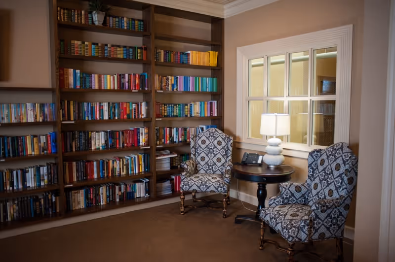 Cozy reading area with built-in bookshelves, two patterned armchairs, and a small table with a lamp.