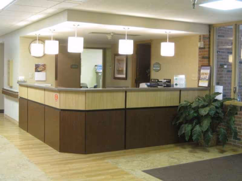 Reception desk area inside a senior living facility lobby with pendant lights and a potted plant.